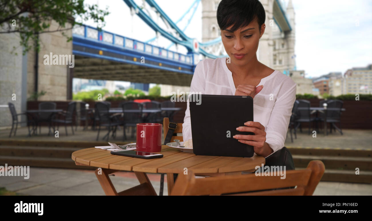 Mixed race female drinking coffee while using tablet near Tower Bridge in London Stock Photo