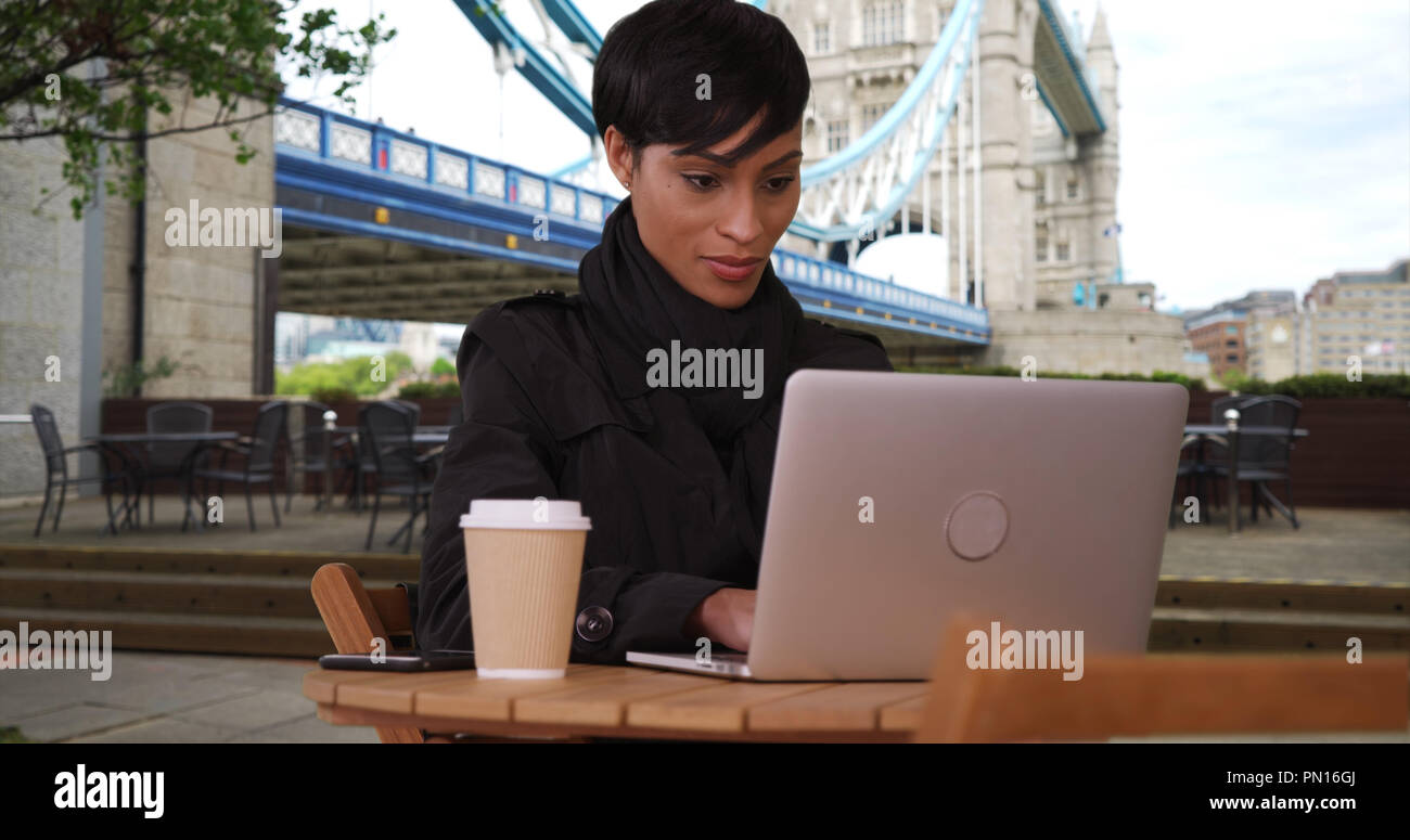 Black female near Tower Bridge in London watches video on laptop outdoors Stock Photo