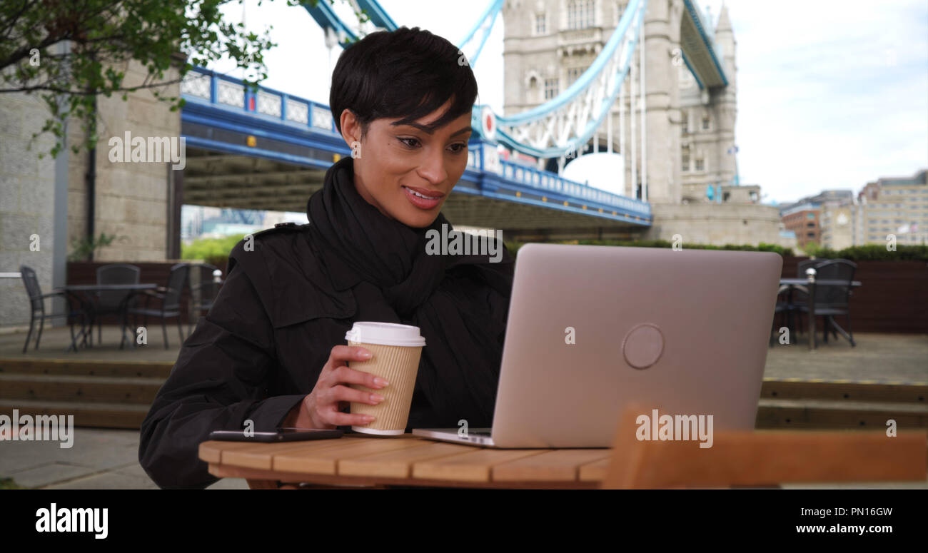Black female near Tower Bridge in London watches video on laptop outdoors Stock Photo