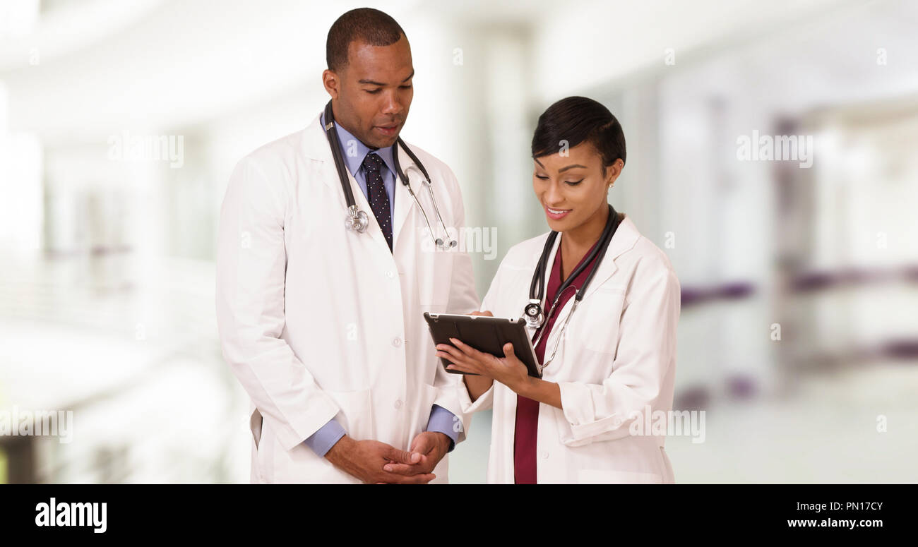 Two professional African American doctors talk while using their tablet Stock Photo