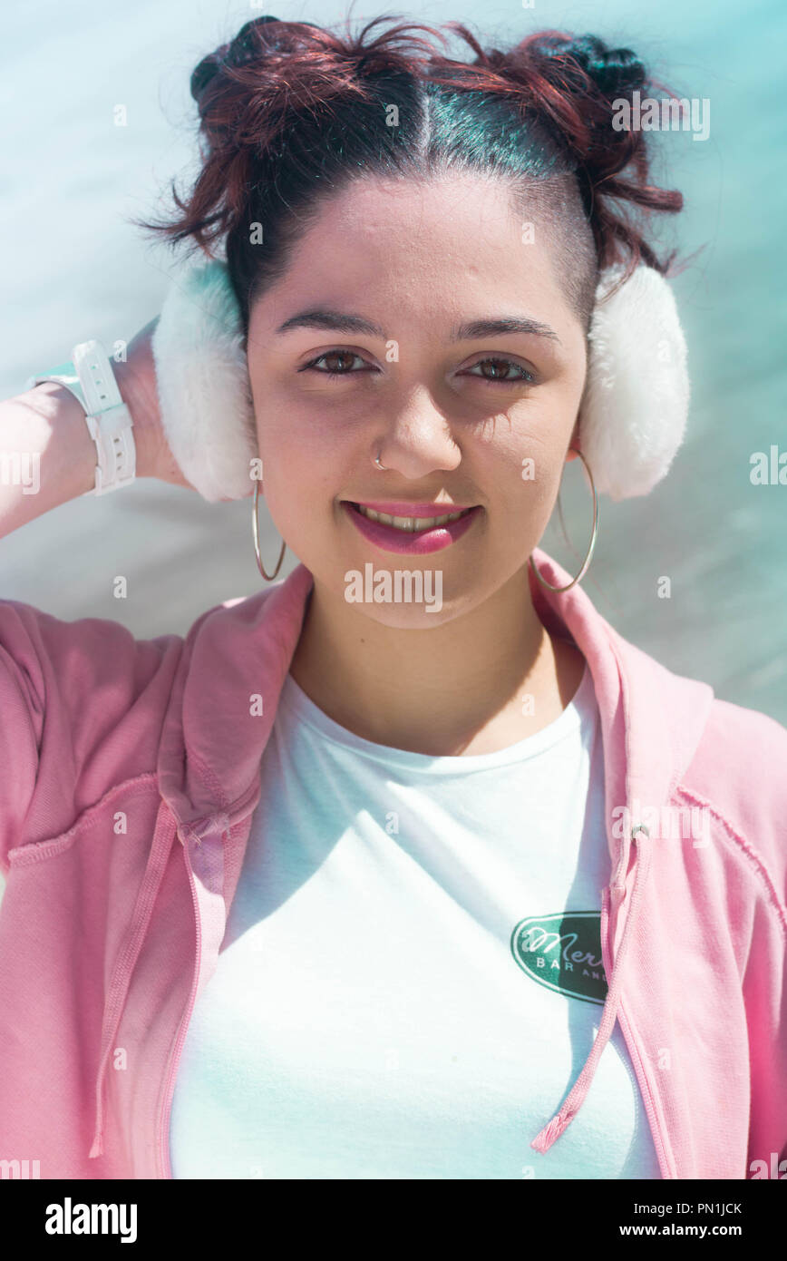 Young brunette woman with two hair buns and white earmuffs and pink jacket Stock Photo