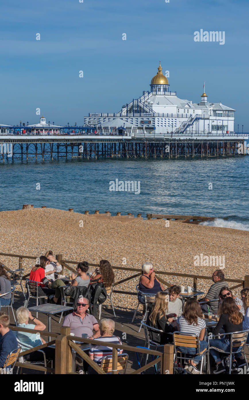 People sitting at an outdoor cafe in Eastbourne, in the county of East Sussex on the south coast of England, with Eastbourne Pier in the background. Stock Photo
