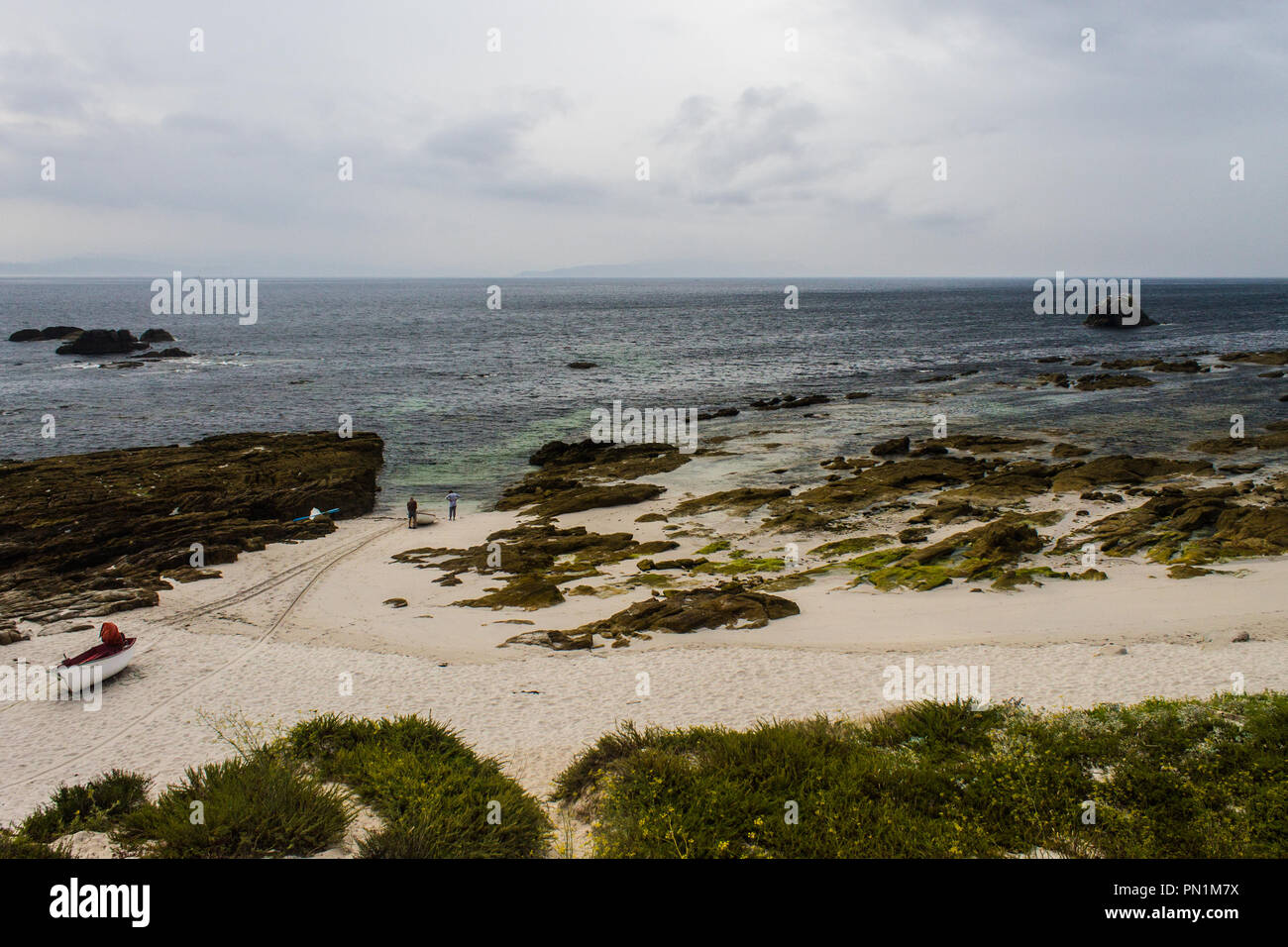 Two men contemplate the sea with a boat nearby. Stock Photo