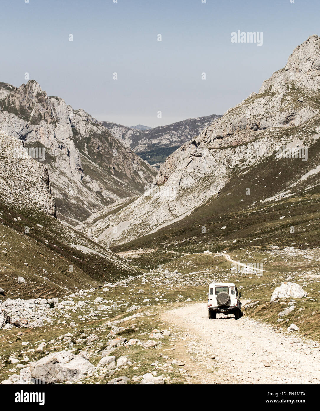 Gravel road along the mountains on a clear day, with an off-road vehicle parked by. Stock Photo
