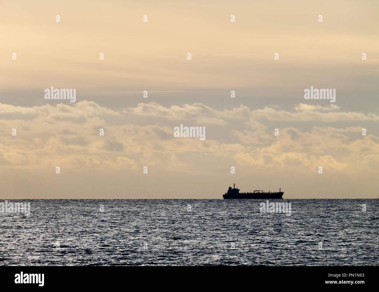 A distant cargo ship is seen on the ocean at the horizon. Stock Photo