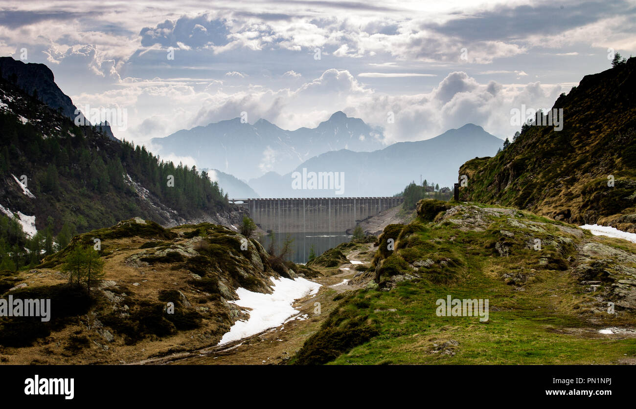 A dam, some snow and a cloud covered mountain range in the background. Stock Photo