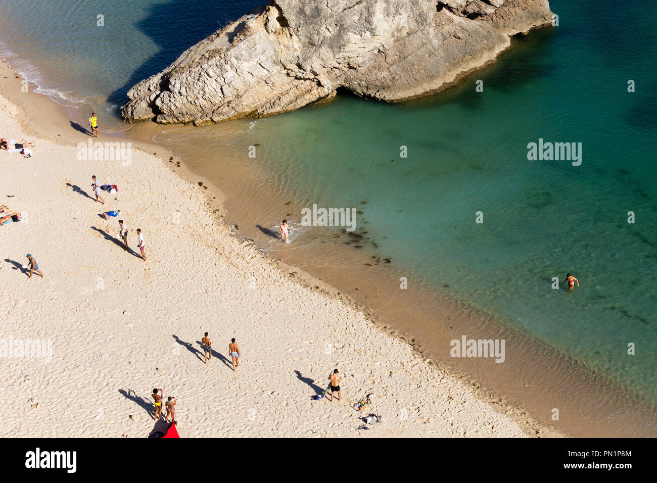 A top-view from several people on the beach with a big rock formation in the ocean. Stock Photo
