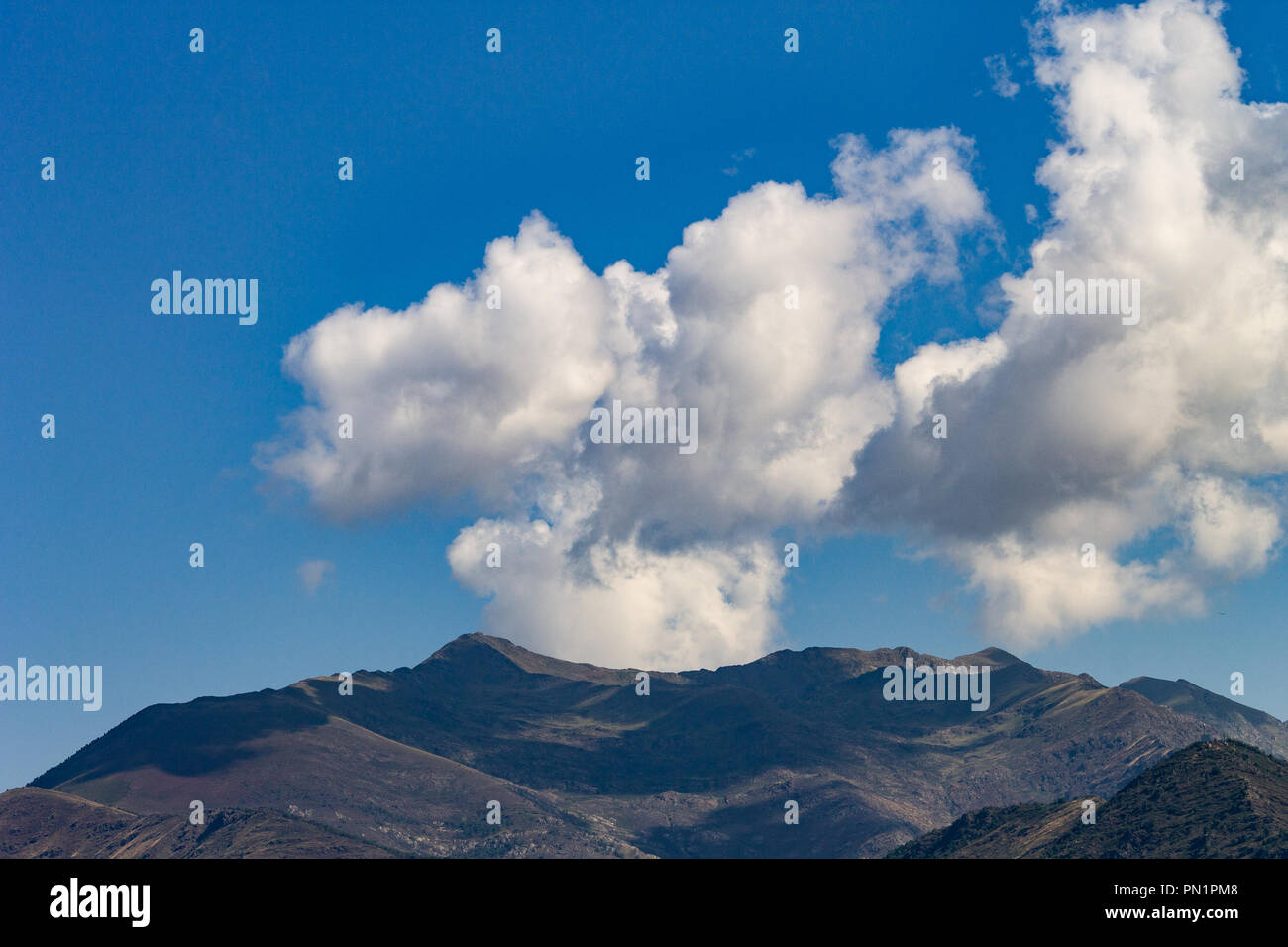 A smoke shaped cloud formation resembling a chimney comes from behind the mountains. Stock Photo
