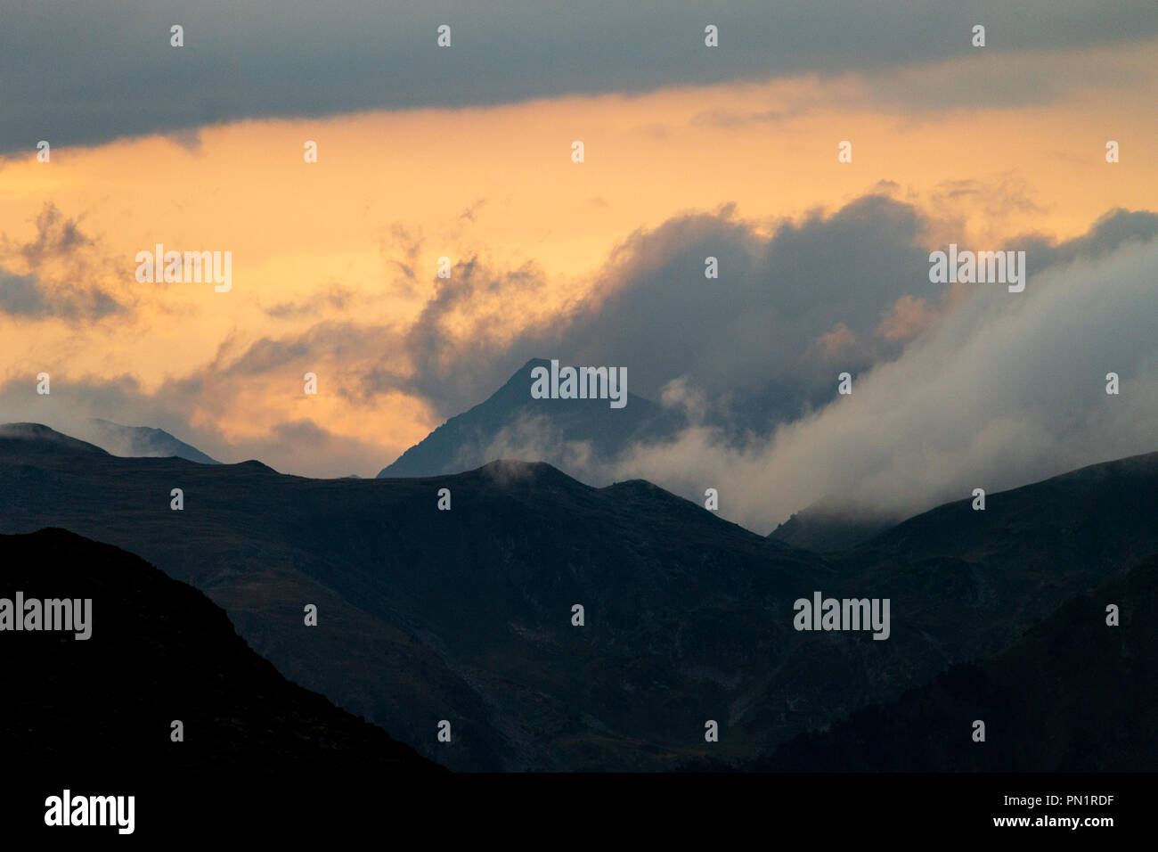 A cloud formation surrounds a mountain top at sunset. Stock Photo