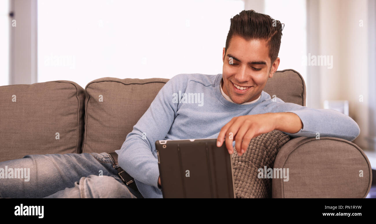 Young Hispanic man sitting on couch using tablet computer in living room Stock Photo