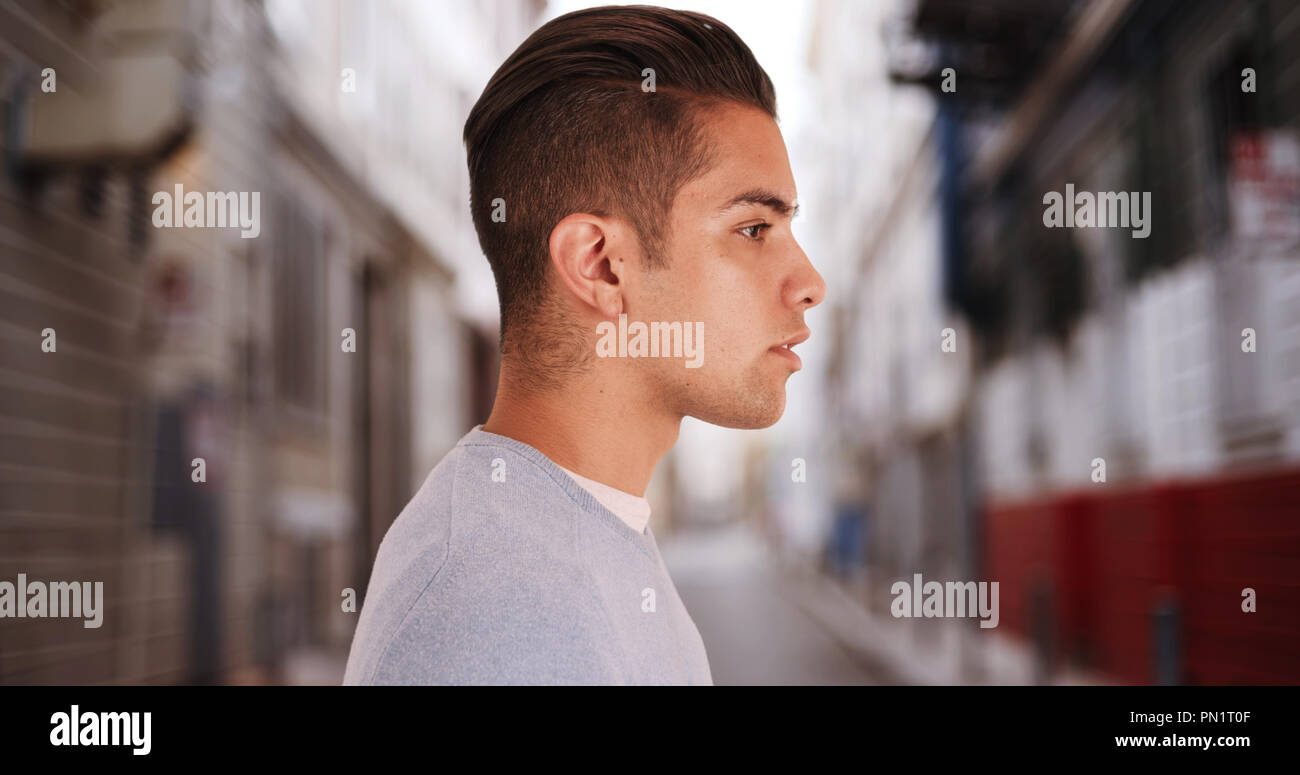 Side view of Hispanic man with cool undercut standing in alley in city Stock Photo