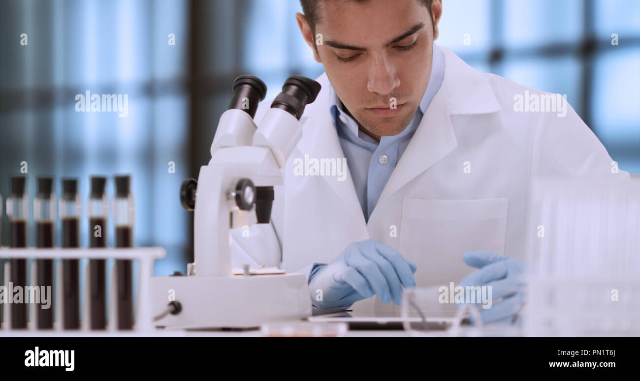 Young Hispanic forensic scientist looking at blood sample through ...