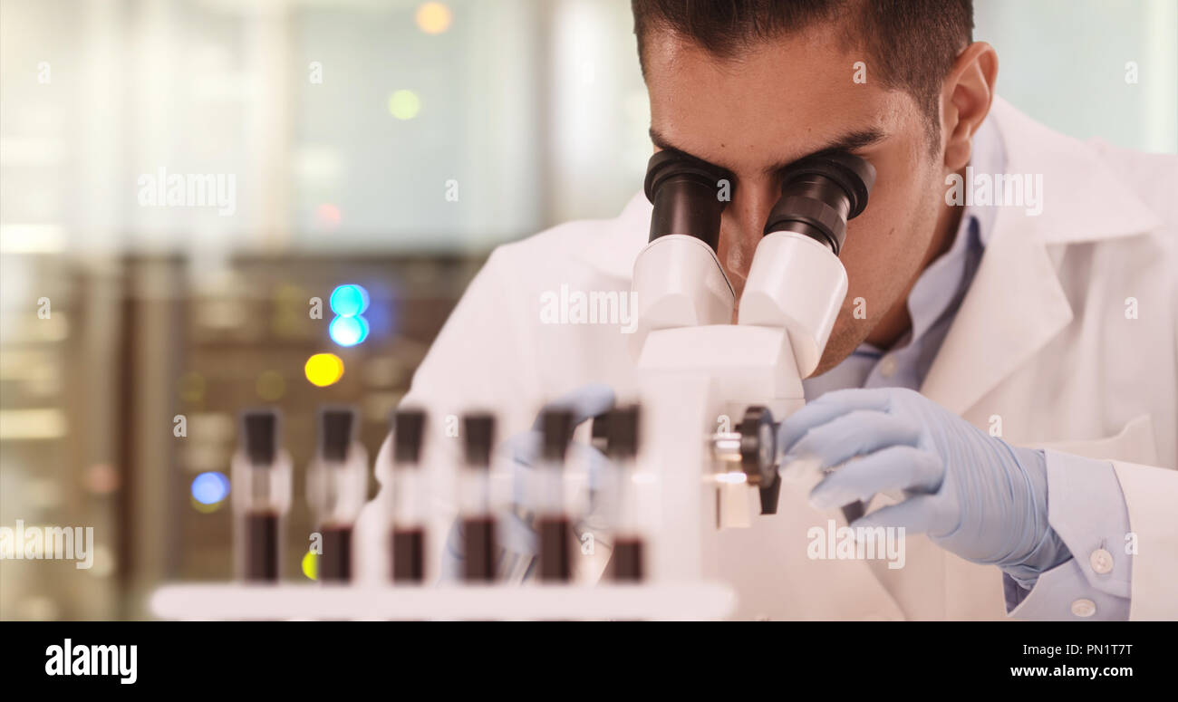 Millennial Hispanic medical research scientist in lab using microscope Stock Photo