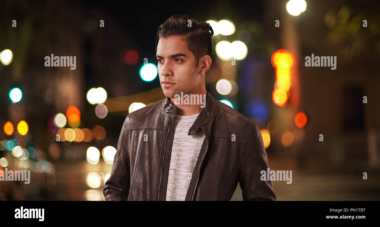 Fashionable millennial Hispanic man standing on city street at night Stock Photo