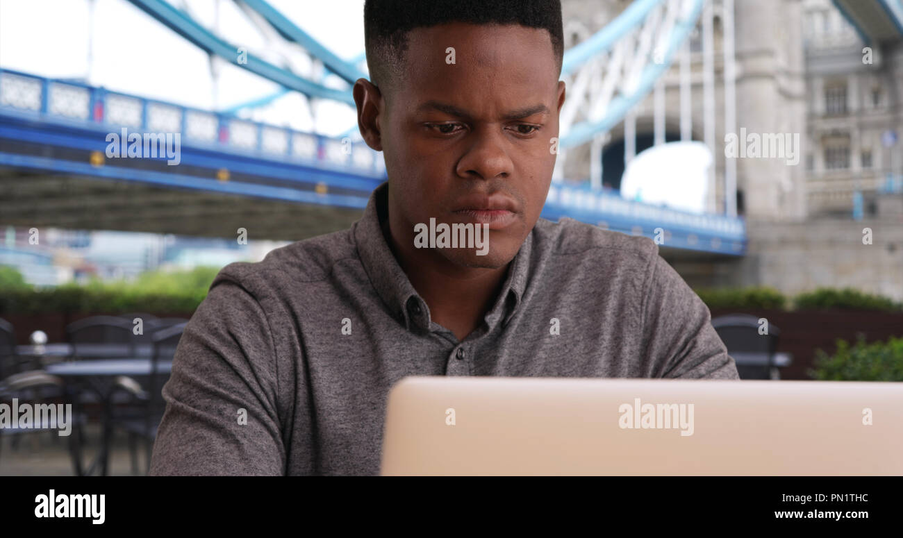 Closeup of young black man sits near Tower Bridge working on a laptop Stock Photo