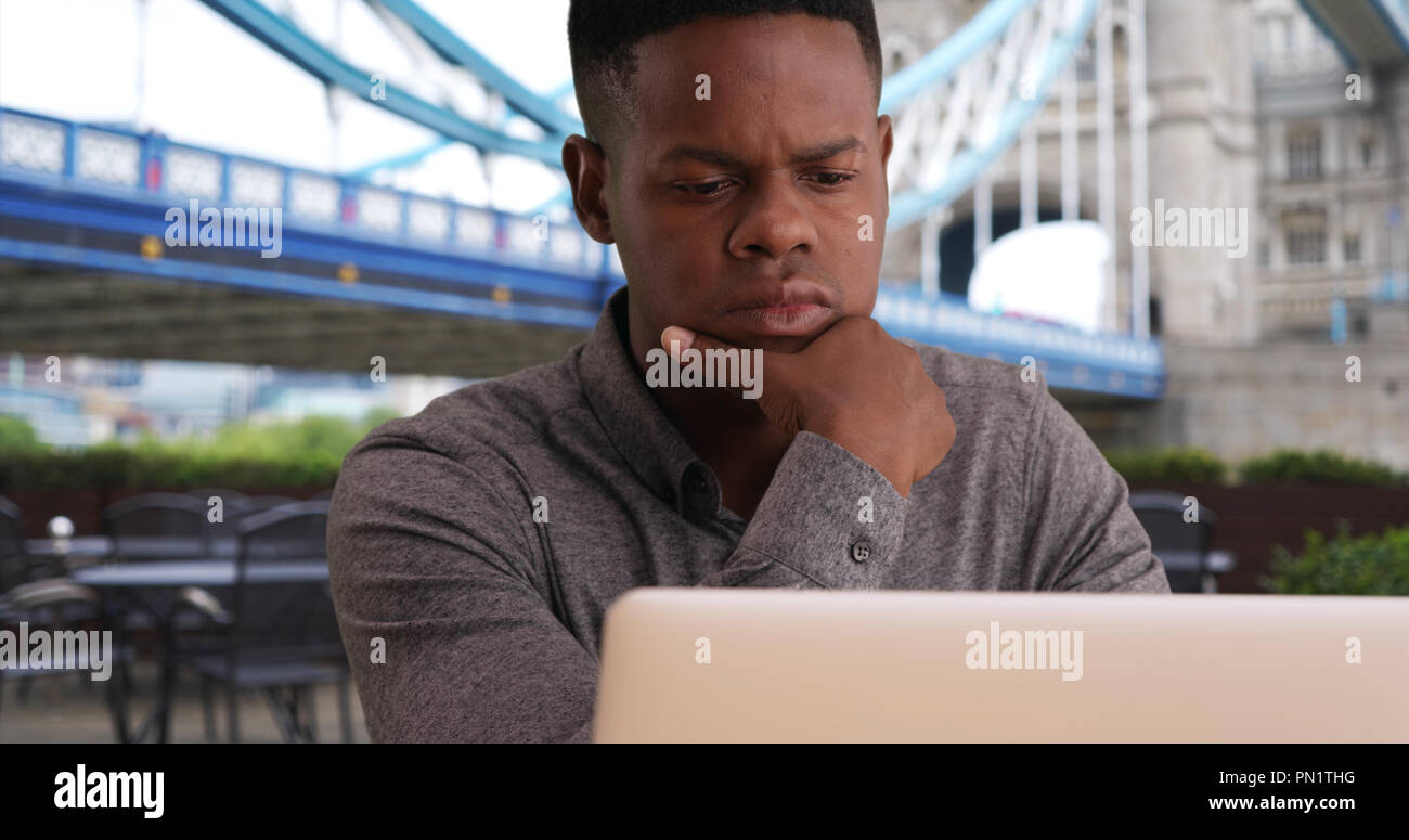 Closeup of young black man sits near Tower Bridge working on a laptop Stock Photo