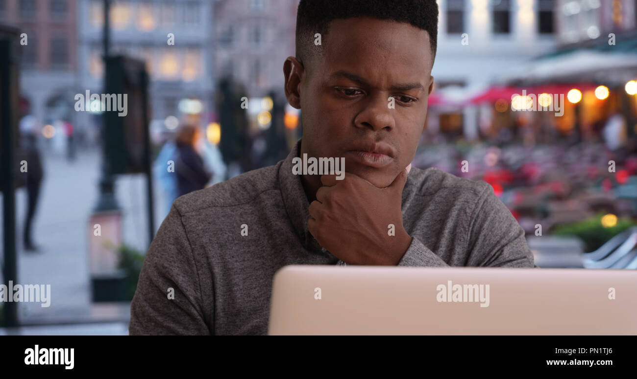 Handsome black male reading emails on laptop computer at outdoors cafe ...
