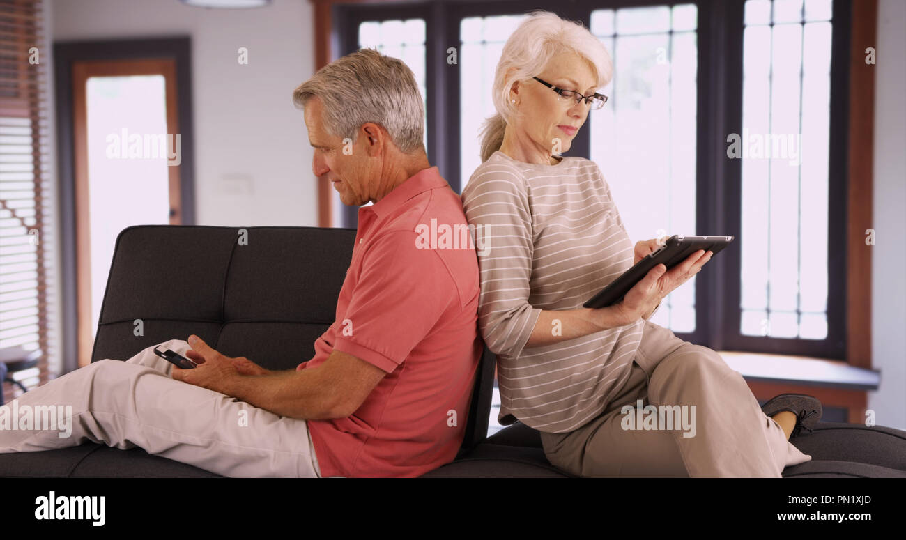 Senior couple using devices on couch at home Stock Photo