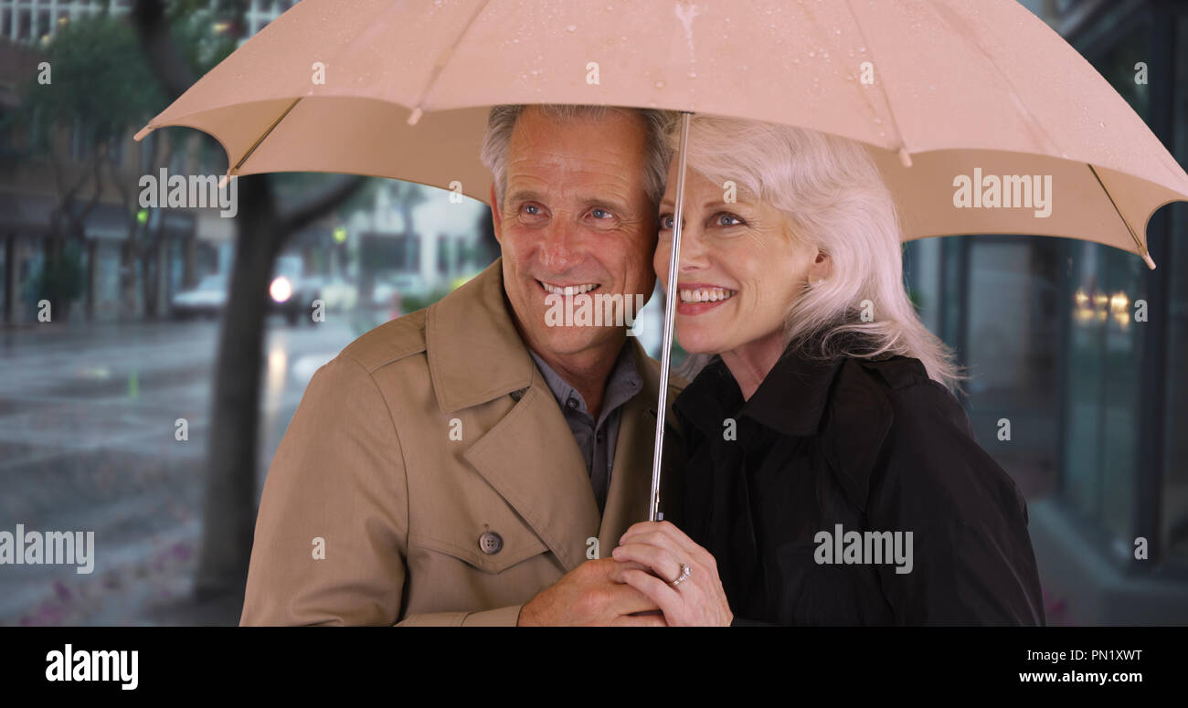 Smiling mature couple standing under umbrella Stock Photo