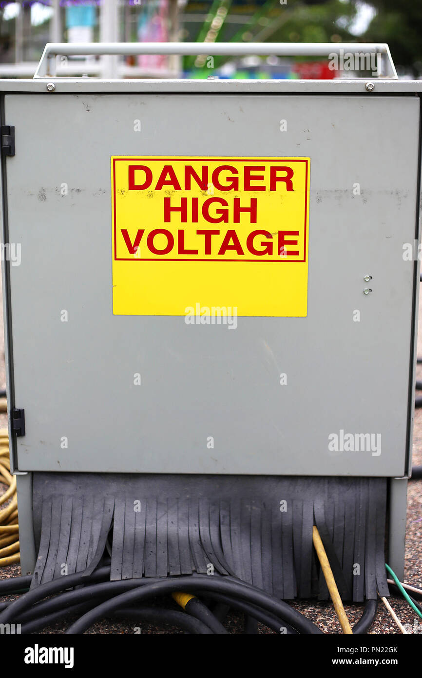 A metal electric power supply junction cabinet box at a carnival has a yellow and red danger high voltage sign on it. Stock Photo