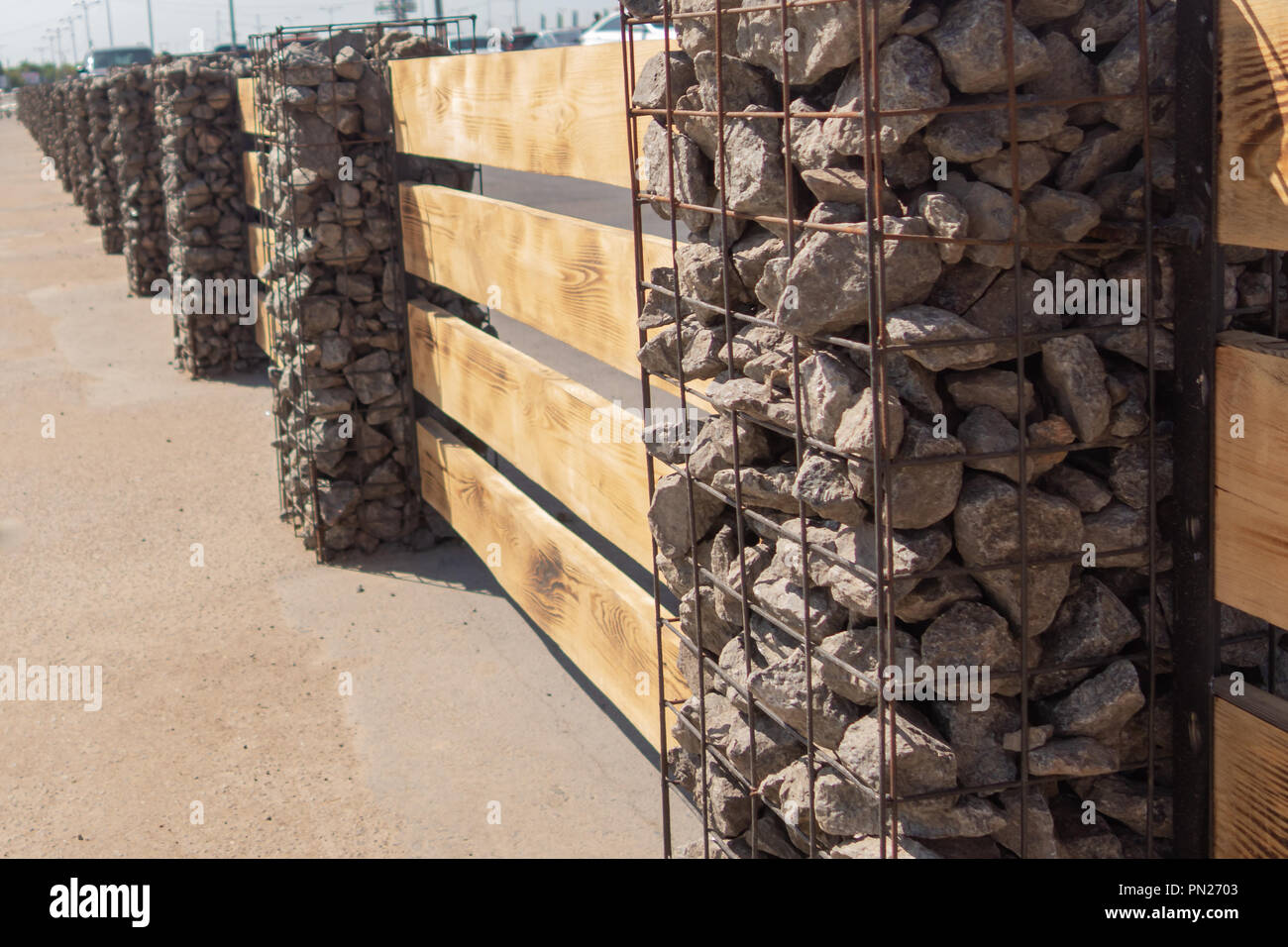 Wooden fence made of horizontal boards with stone pillars. The pillars are made of a metal frame with granite gravel embedded in it. Option of decorat Stock Photo