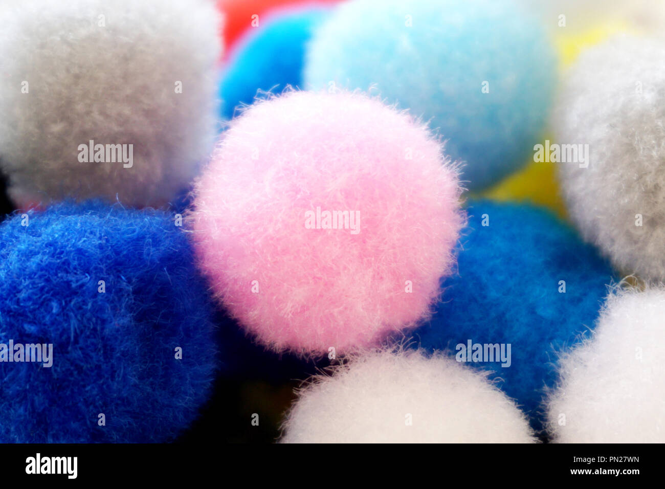 Colorful fluffy wool pom poms with one pastel pink on the top Stock Photo