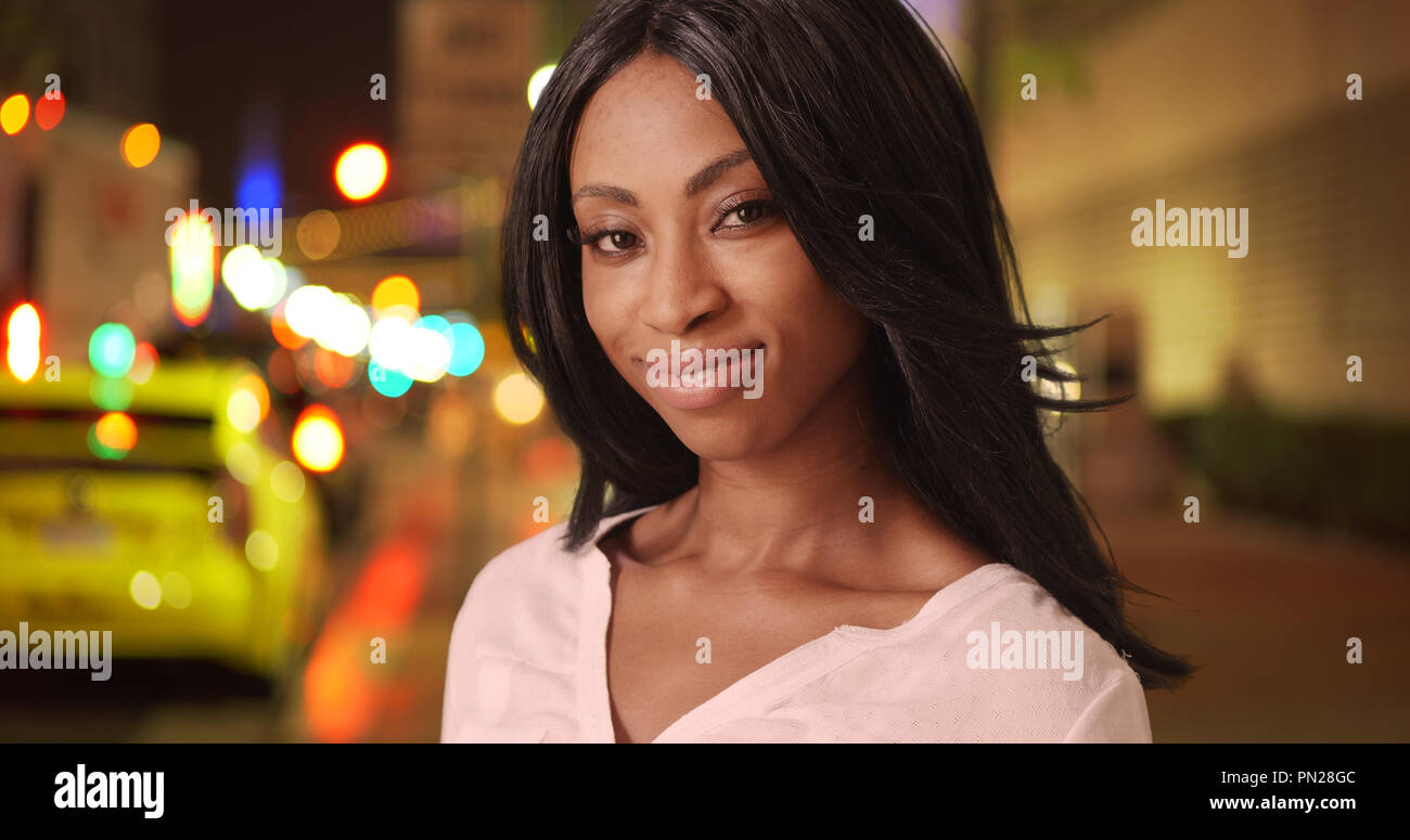 Happy black woman smiling on city street at night Stock Photo