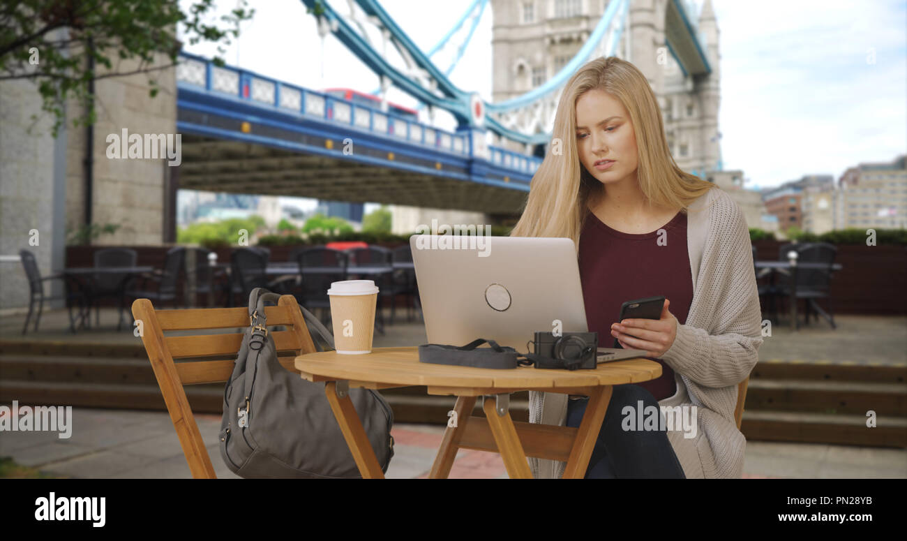 Attractive white girl in London uses laptop and smartphone near the Tower Bridge Stock Photo