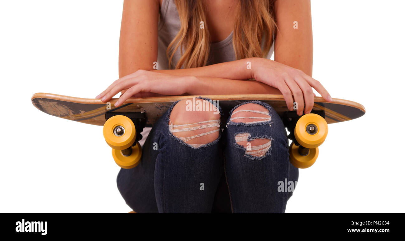 Female wearing ripped jeans and a tank top sitting holding skateboard Stock Photo