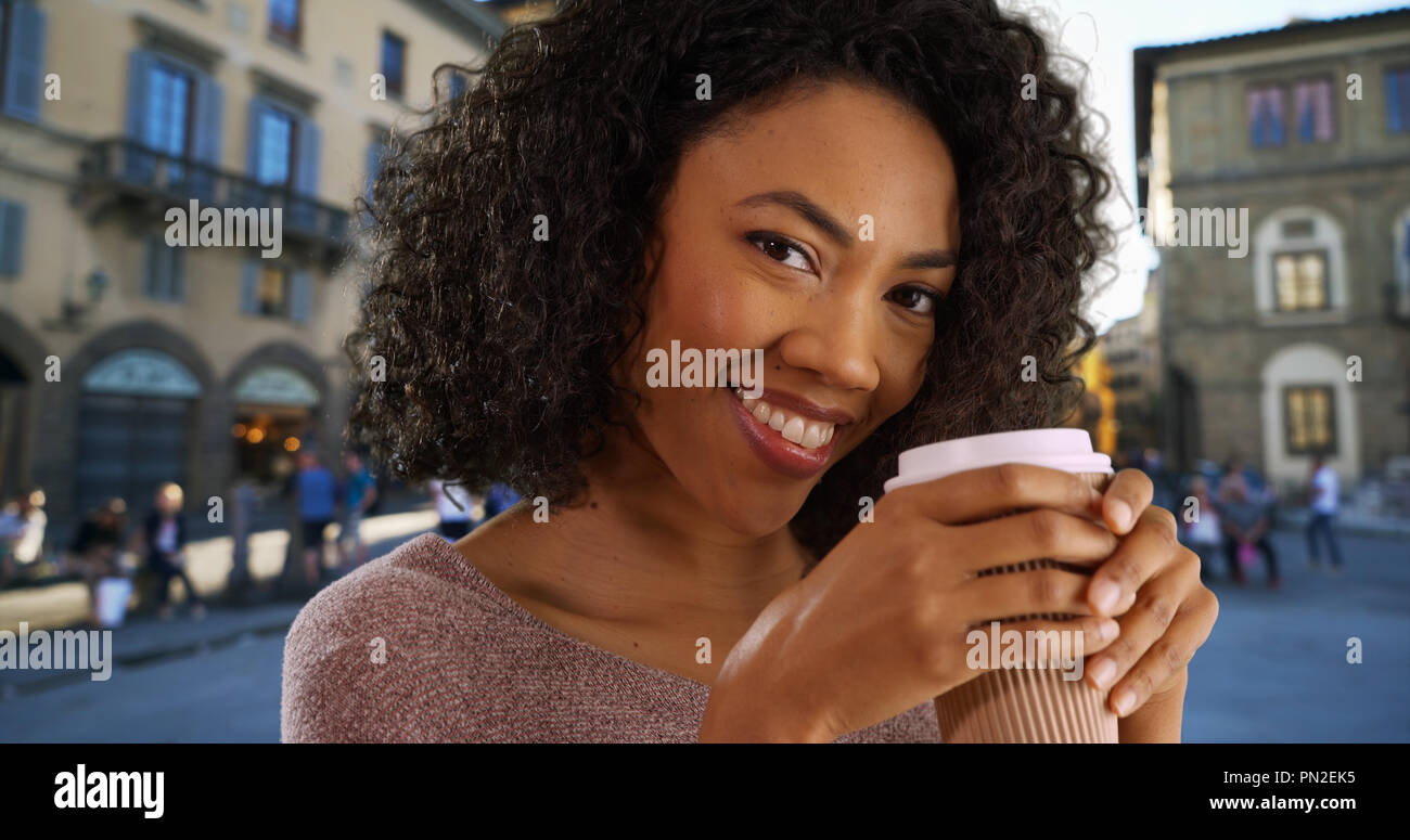 Happy young black woman drinking coffee in town square out of paper to ...