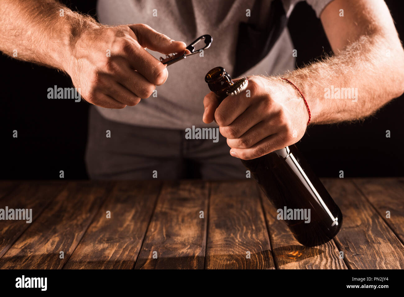cropped image of man opening beer bottle by opener at wooden table Stock Photo