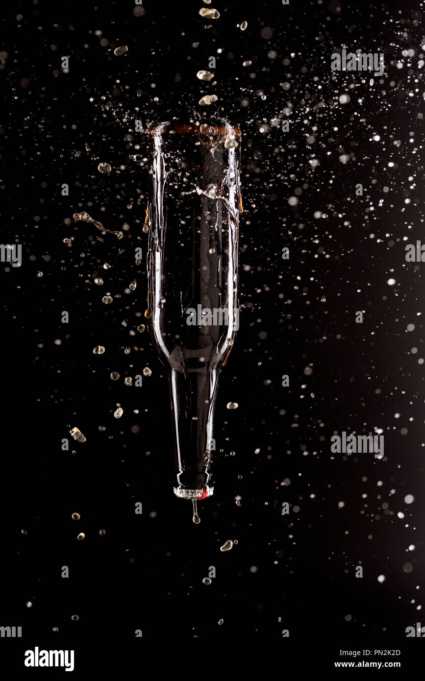 beer bottle upside down with splashes around isolated on black