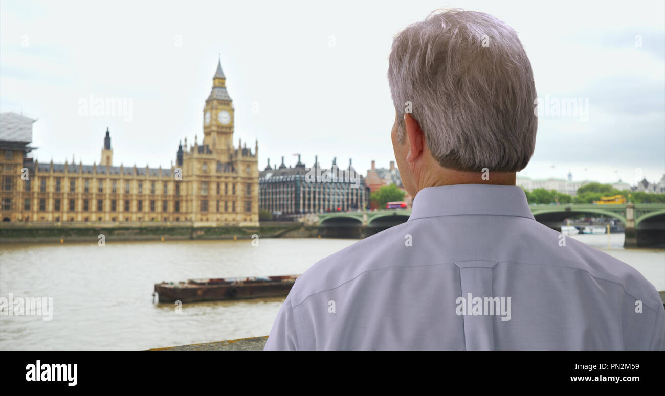 Older White Man In London Looks On At Big Ben Over River Thames Stock older-white-man-in-london-looks-on-at-big-ben-over-river-thames-stock