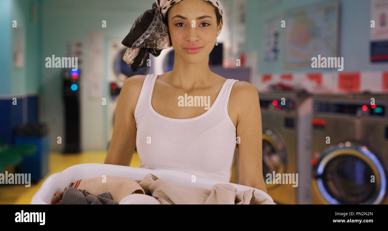 Attractive Latin female holds basket of dirty clothes smiling at camera Stock Photo