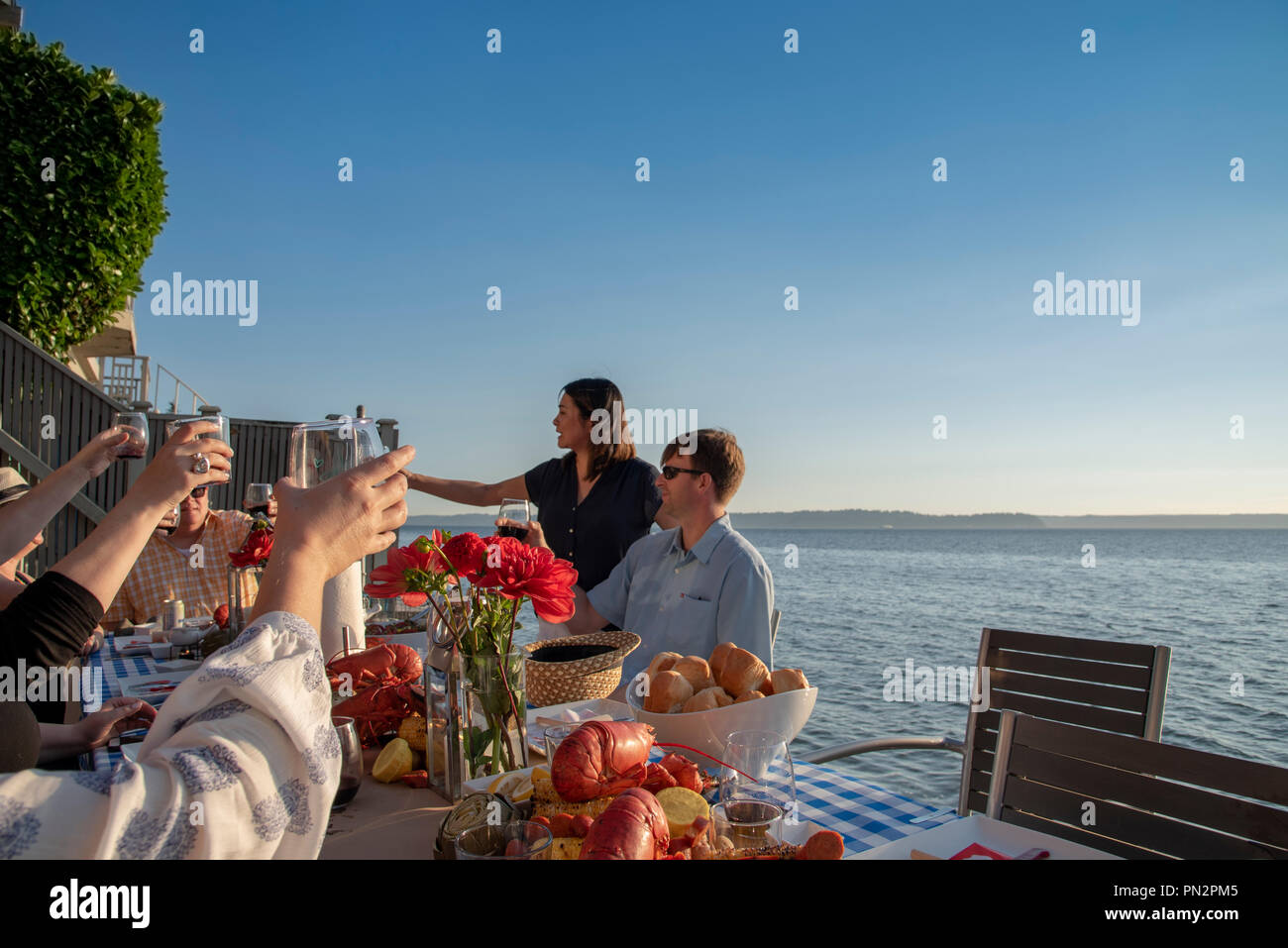 Group of friends raising glasses at a seafood dinner seaside in late afternoon sun. Stock Photo