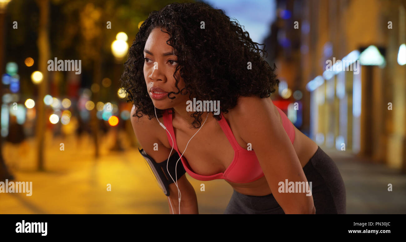 Black woman runner taking break while on a run in the city at night Stock Photo