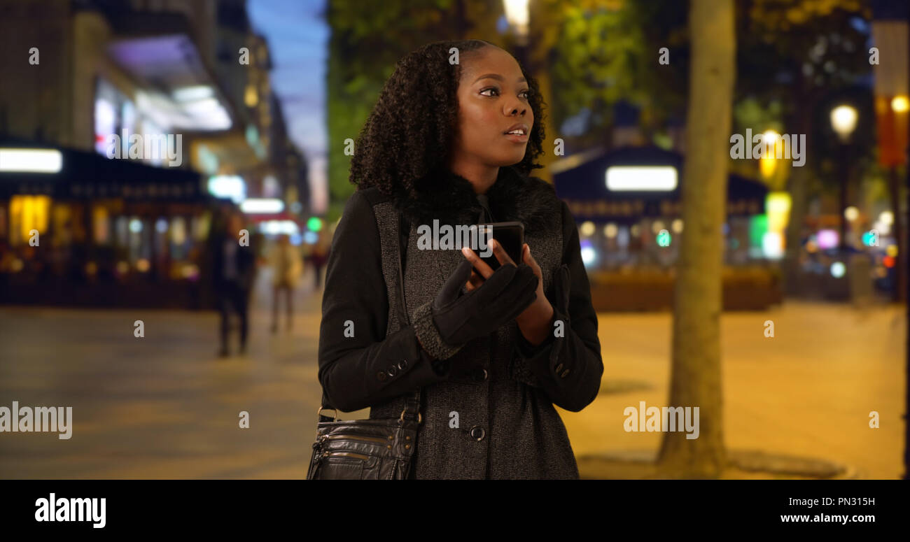 Pretty black woman standing on city street at night looking off screen ...