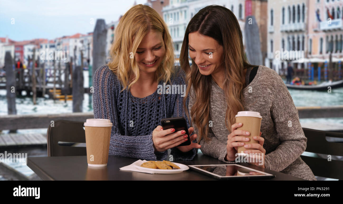 Couple of attractive girls sitting and using on smart phone by Venetian canal Stock Photo