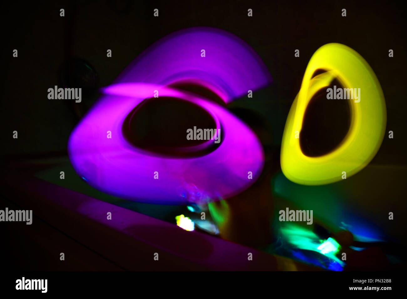 Boy playing in the bathtub making a light painting with glow sticks Stock Photo