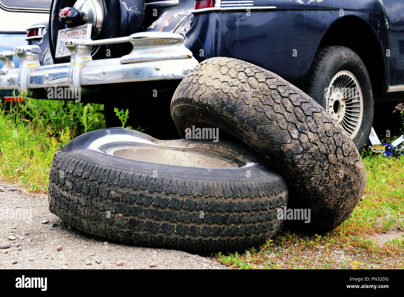 Old flat tires next to a vintage car in a state of repair Stock Photo