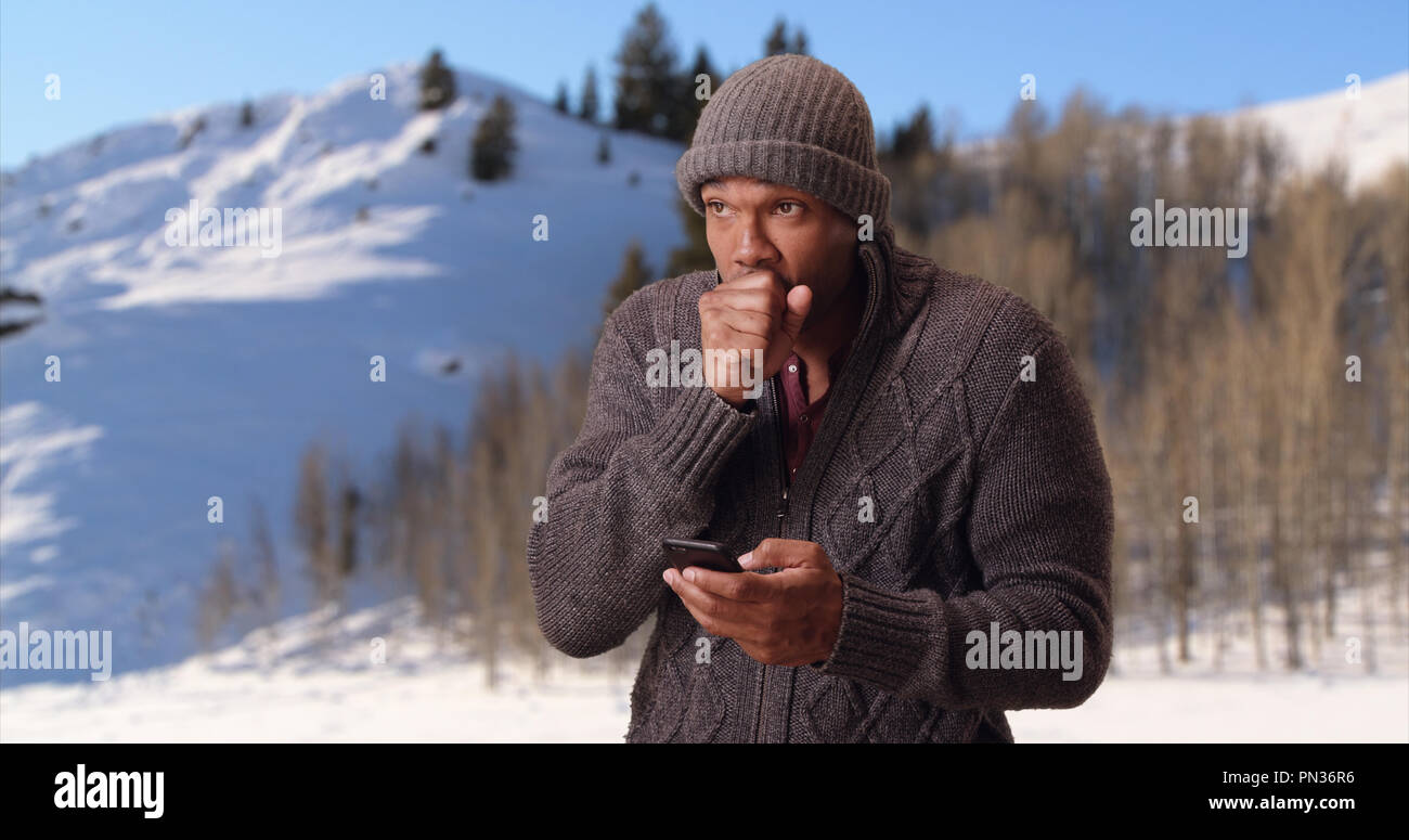 An African American man stands trembling in the icy tundra on his smart phone Stock Photo