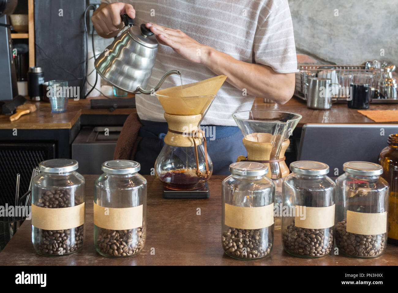 barista holding drip pot and pouring water onto ground coffee beans in the paper filter for brewing drip coffee at the cafe in the morning. coffee dri Stock Photo