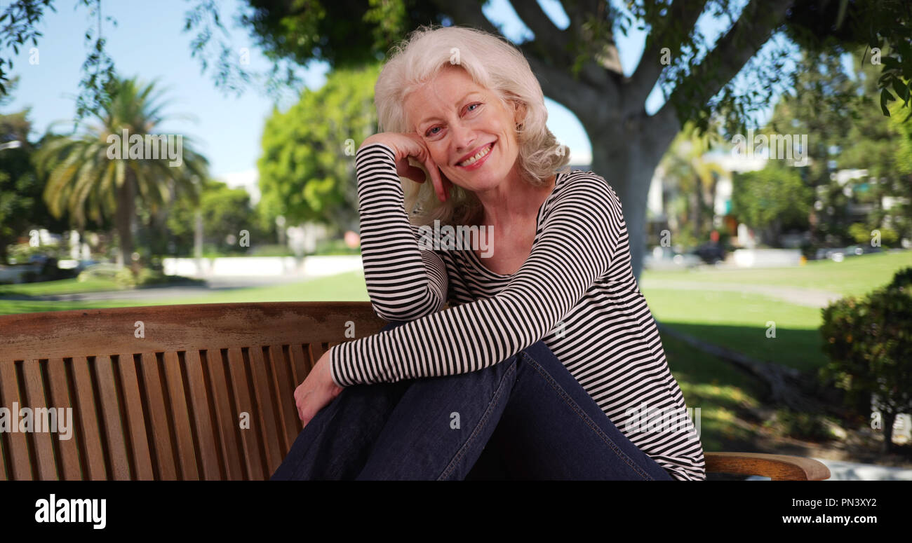 Old woman with happy expression on her face posing on bench on nice day the park Stock Photo