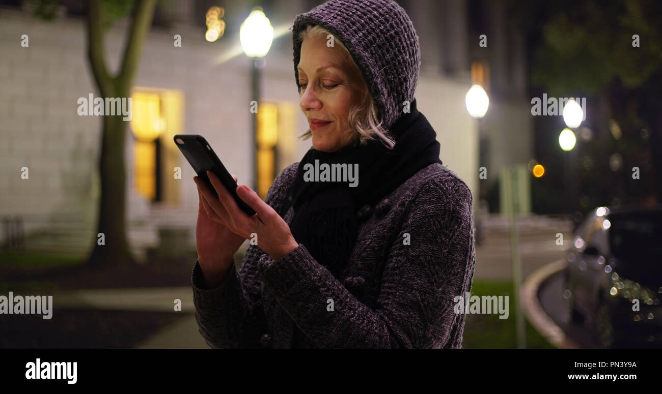 Caucasian senior woman on mobile device standing outside on quiet night ...