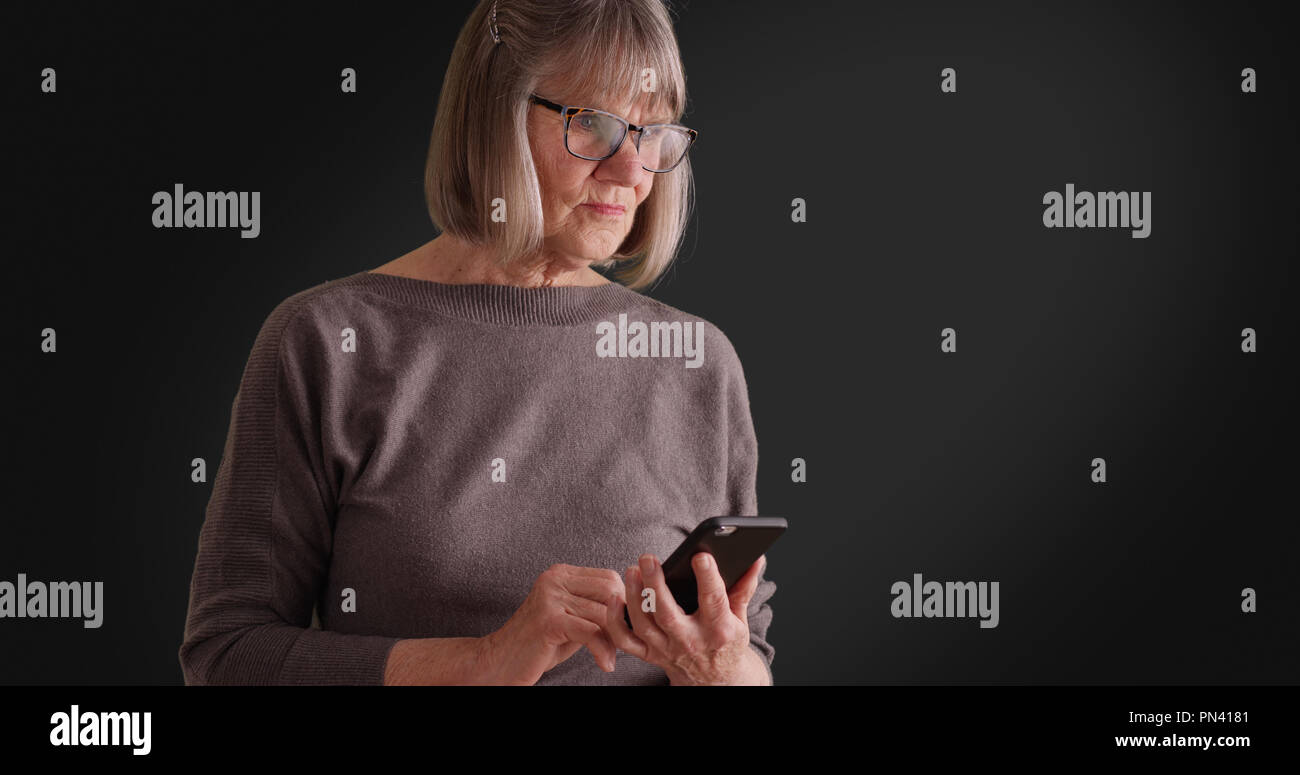 Somber lady reading worrying message on mobile device on dark gray background Stock Photo