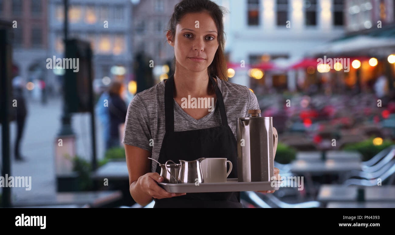 Unhappy waitress wearing apron and carrying tray with coffee at outdoor cafe Stock Photo