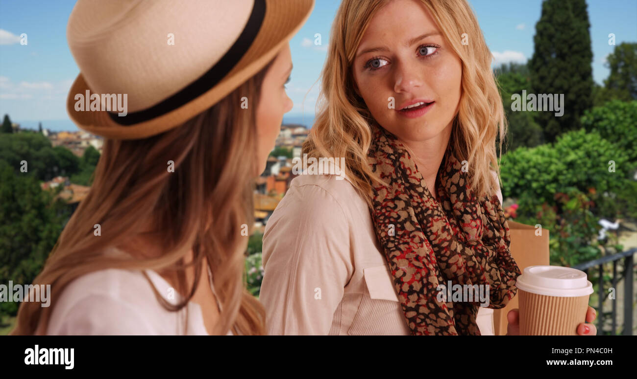 Fashionable blonde female with coffee talking with friend outside in Florence Stock Photo