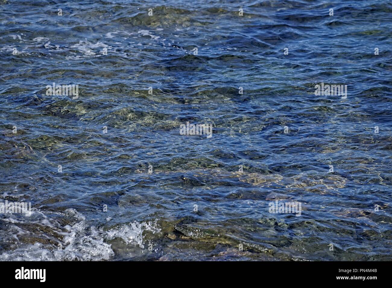 Textured ripples on the surface of the shallow water, at a beach. Rocks showing just below the surface. Stock Photo