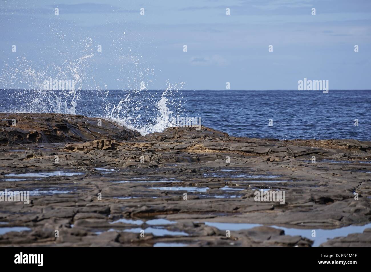 Looking across a rock platform, or shelf, at the sea and sky, with a wave splashing against the edge. Stock Photo