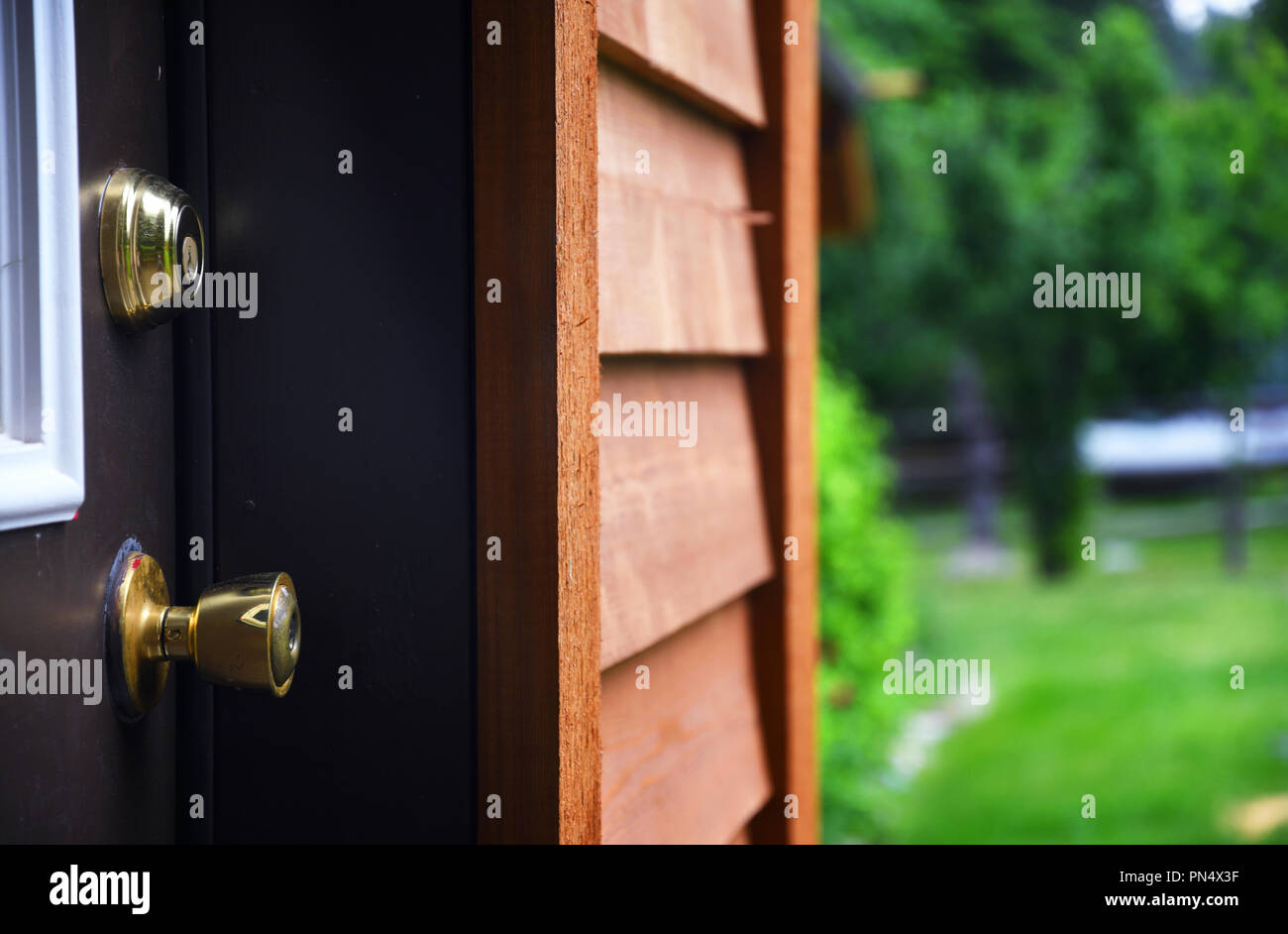Close up of a door knob and dead bolt with cedar house siding and a lawn in the background Stock Photo